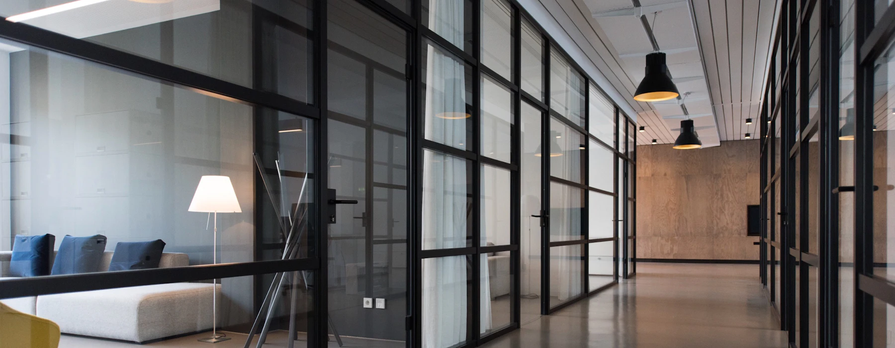 A quiet modern office corridor lined with glass-walled meeting rooms