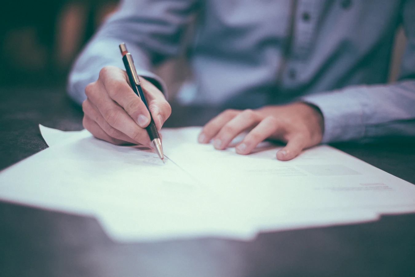 Hands in shirt sleeves holding a pen over printed documents on a desk